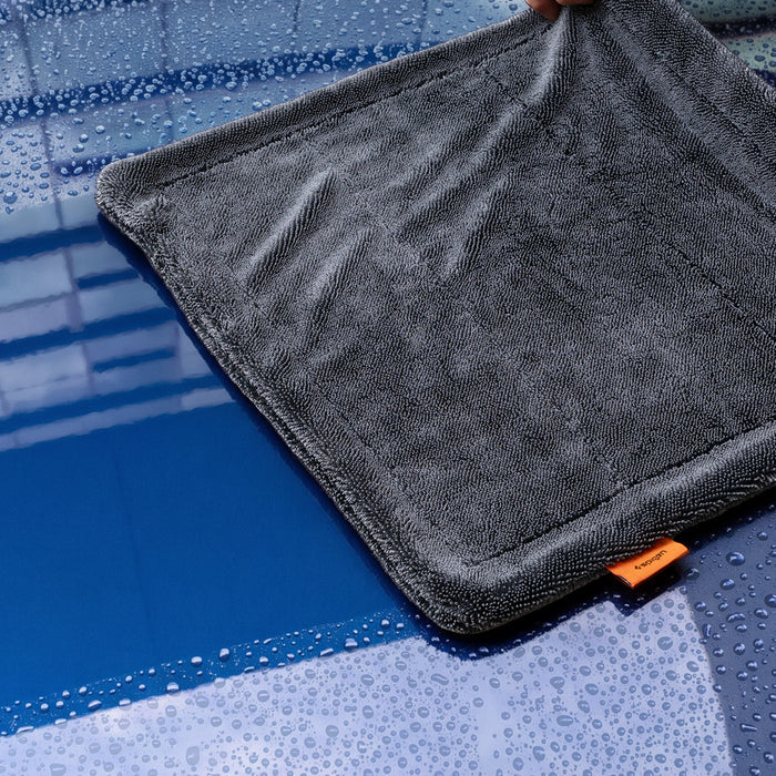 ACP11389 - Hand holding up the corner of a gray Spigen microfiber towel over a wet, water-splashed surface