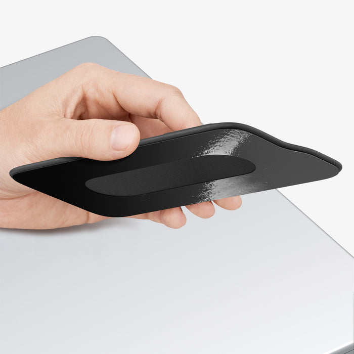 APP11228 - SSD/HDD Holder | LD221 in Black showing hand pressing flat against MacBook lid with adhesive backing partially removed for placement